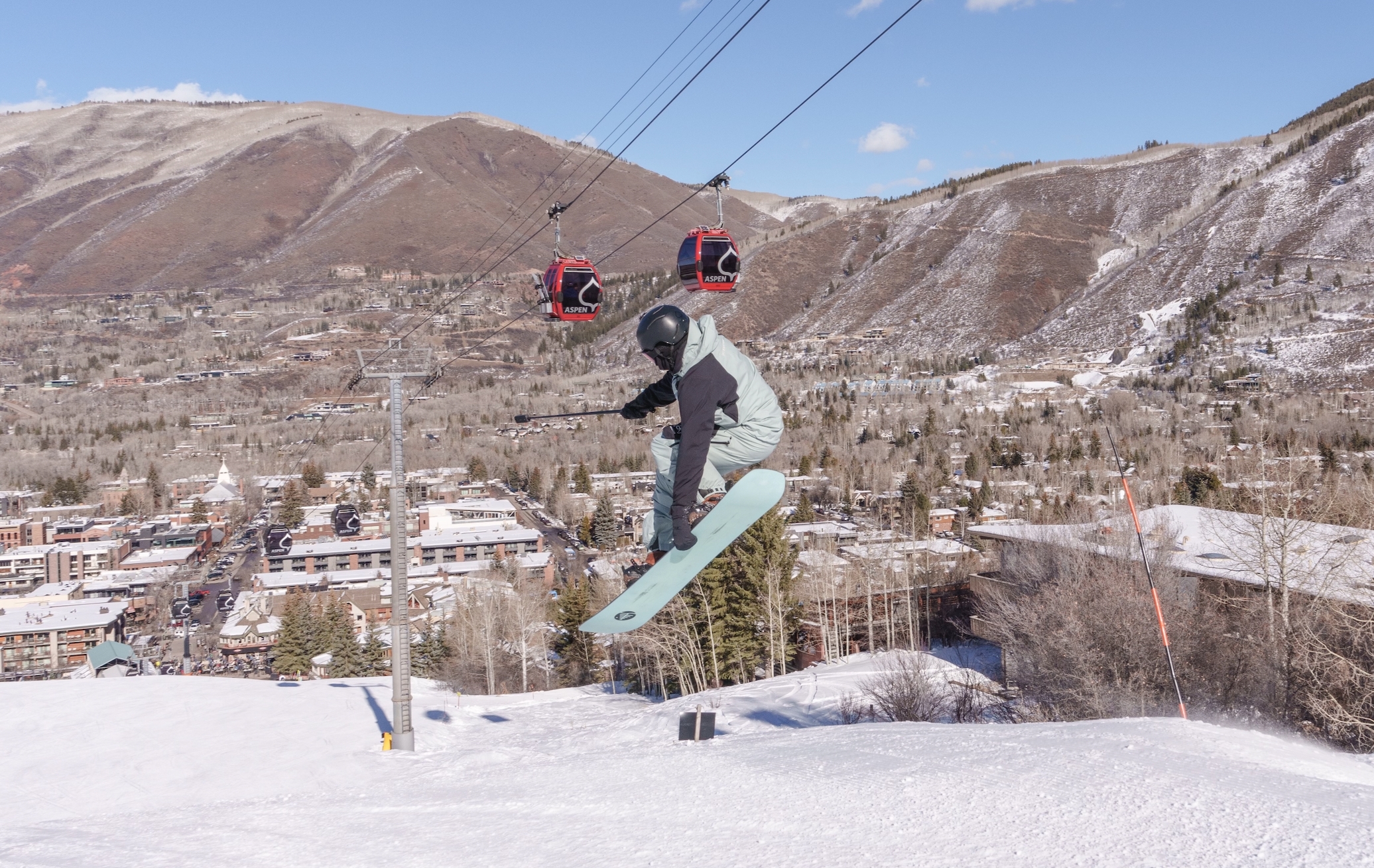 A snowboarder at Aspen Snowmass jumping down a mountain holding Insta360 X4 and the Insta360 Invisible Selfie Stick out in front of themselves.